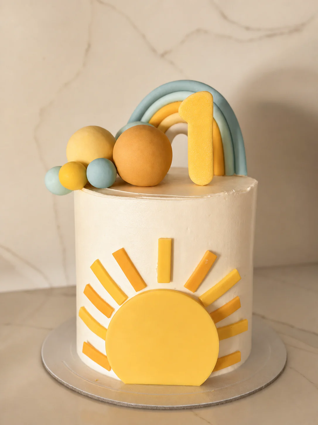 Bolo personalizado de primeiro aniversário em tons creme, mel e azul com arco-íris e sol
